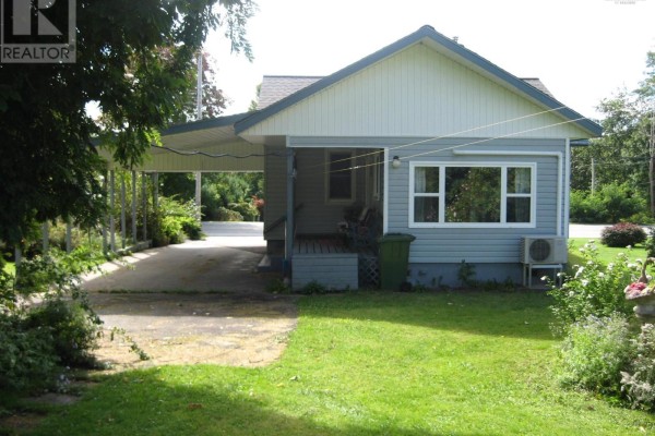Side view of a light blue single-story house with a carport and green lawn. - 103 Highway 8, Milton