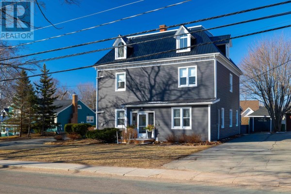 Front view of a dark grey multi-family home with white trim, dormer windows, and a paved driveway. - 103 Olde Brighton Lane, Charlottetown