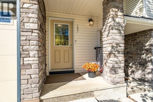 Entrance to the townhouse with stone pillars, a beige door, and a potted plant. - 103 Panatella Road Nw, Calgary