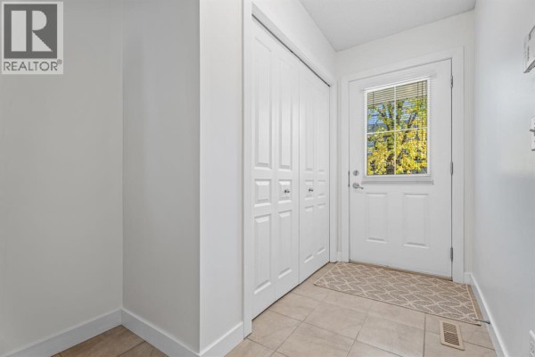 Interior entryway with tiled floor, white bi-fold doors, and a back door with windows. - 103 Panatella Road Nw, Calgary
