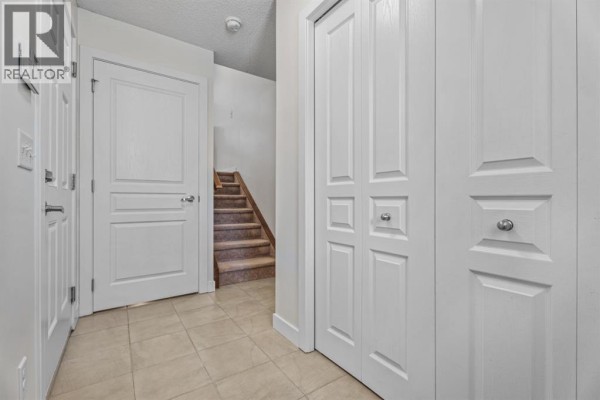 Hallway with tiled floor, white doors, and a staircase leading upstairs. - 103 Panatella Road Nw, Calgary