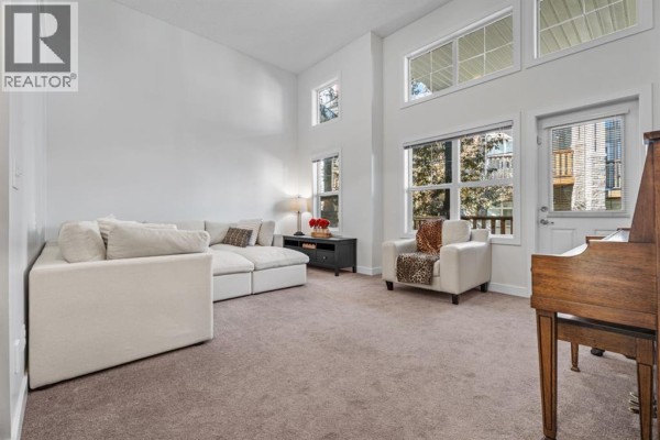 Living room with a large sectional sofa, armchairs, a piano, and high ceilings with windows. - 103 Panatella Road Nw, Calgary