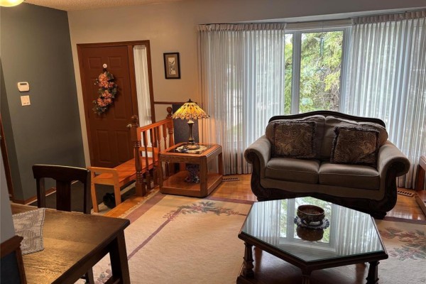 Living room with a brown sofa, armchair, coffee table, and a bay window with sheer curtains. - 103 Pear Tree Bay, Winnipeg