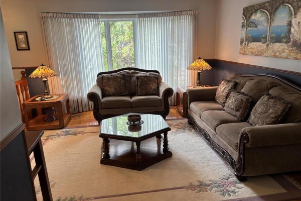 Living room featuring two sofas, a coffee table, two side tables with lamps, and a bay window. - 103 Pear Tree Bay, Winnipeg