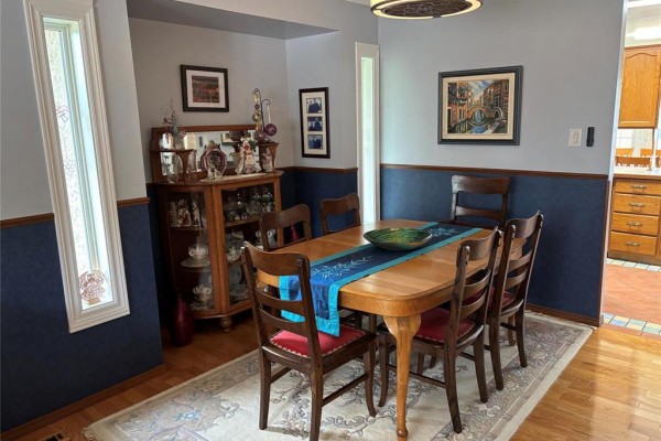 Dining room with a wooden table, six chairs, a display cabinet, and a window with decorative glass. - 103 Pear Tree Bay, Winnipeg