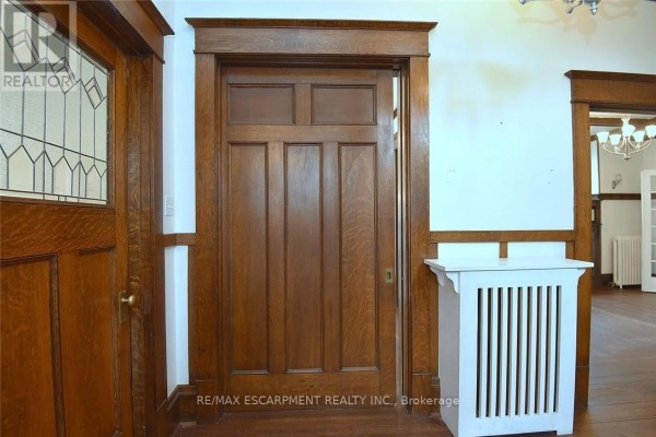 Interior hallway featuring a solid wood door, white radiator cover, and wood trim. - 103 Sherman Avenue S, Hamilton
