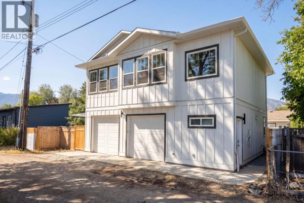 Bright open-concept kitchen and living area with white cabinets, a large island, stainless steel appliances, and dining table. - 1030 Timmins Street, Penticton