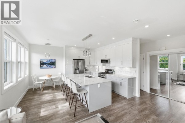 Kitchen area with white high-gloss cabinets, a quartz island, stainless steel appliances, and a view through the windows. - 1030 Timmins Street, Penticton