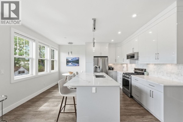 Interior staircase with light wood treads, glass railing, and white walls, leading to the upper level. - 1030 Timmins Street, Penticton