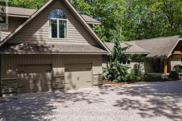 The front of a house showing a two-car garage with beige doors and stone accents. - 10308 Beach O' Pines Road, Lambton Shores