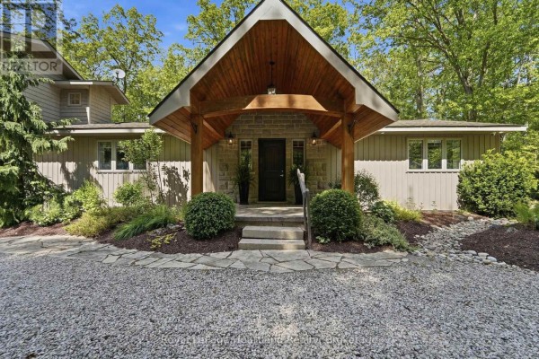 The covered entrance of a beige house with stone accents and stone steps. - 10308 Beach O' Pines Road, Lambton Shores