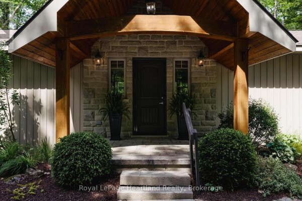 Close-up of a dark front door with stone surround, flanked by plants and stone steps. - 10308 Beach O' Pines Road, Lambton Shores