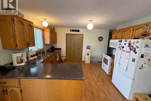 Kitchen area with a sink, countertops, wooden cabinets, and a water cooler. - 10313 89 Street, Peace River