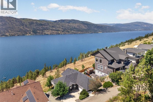 Aerial view of a multi-story house on a slope with a large blue lake and mountains behind. - 10326 Nighthawk Road, Lake Country