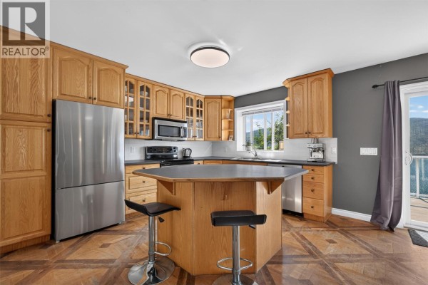 Kitchen with light wood cabinets, stainless steel appliances, an island with bar stools, and dark gray walls. - 10326 Nighthawk Road, Lake Country