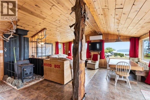 Living area with wood stove, TV, dining table, and view of water through large window. - 1033 Seventh Ave, Ucluelet