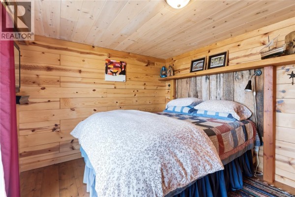 Bedroom with a queen-size bed, wood-paneled walls, and a quilt on the bed. - 1033 Seventh Ave, Ucluelet