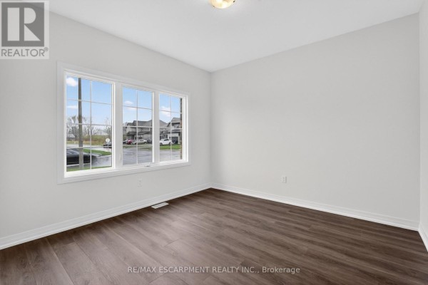 Empty room with white walls, dark wood-look flooring, and three large windows overlooking a street. - 1034 Kraft Road N, Fort Erie