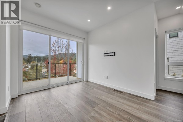 Empty room with large sliding glass doors opening to a balcony and distant view. - 1036 Boxcar Close, Langford