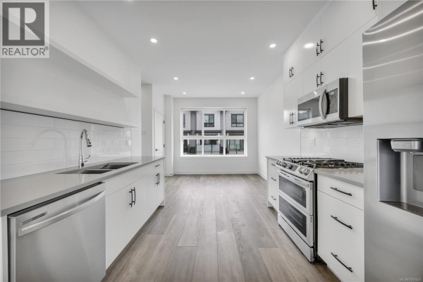 Modern white kitchen with stainless steel appliances and grey quartz countertops. - 1036 Boxcar Close, Langford
