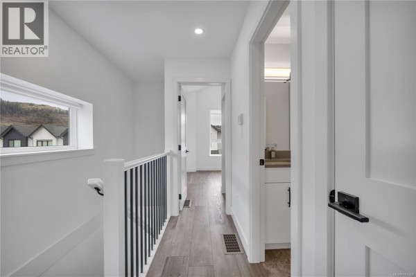 Hallway on the upper floor with a view of a bathroom and staircase railing. - 1036 Boxcar Close, Langford