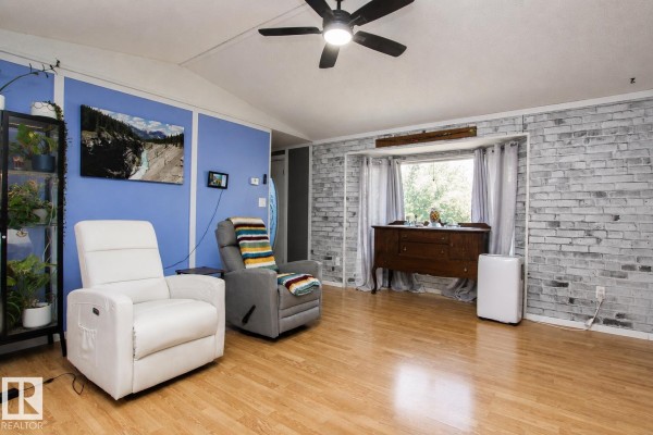 Living room with light wood floors, white brick accent wall, and two recliners near a bay window. - 1036 Lakeland Cr, Sherwood Park