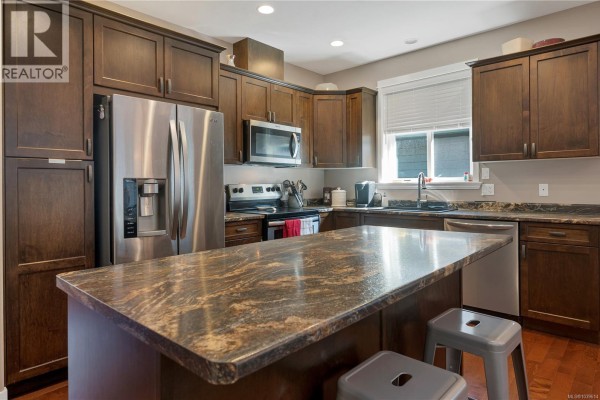 Kitchen featuring dark wood cabinets, stainless steel appliances, and a large granite island. - 1037 Cordero Cres, Campbell River