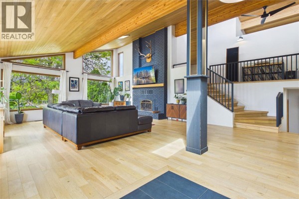 Living room with leather sofa, wood-paneled ceiling, large windows, and fireplace. - 10371 Okanagan Centre Road E, Lake Country