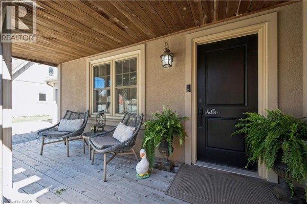 Covered porch with two chairs, a small table, plants, and a black front door with "hello" decal. - 1039 Molesworth Street, Wellesley