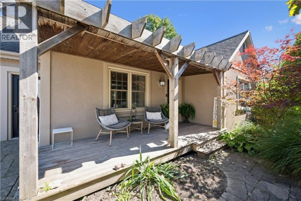 Front porch with wooden floor and pergola, seating area, and lush greenery surrounding the entrance. - 1039 Molesworth Street, Wellesley