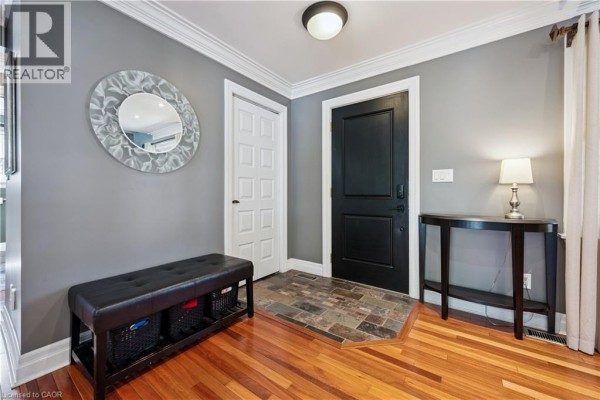 Foyer with grey walls, hardwood floors, a black door, a bench, and a console table with a lamp. - 1039 Molesworth Street, Wellesley