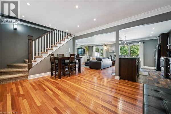 Open-concept living, dining, and kitchen area with hardwood floors, a staircase, dark cabinetry, and large windows. - 1039 Molesworth Street, Wellesley