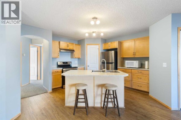 Kitchen with light wood cabinets, stainless steel appliances, and a central island with two stools. - 104, 23 Everridge Square Sw, Calgary