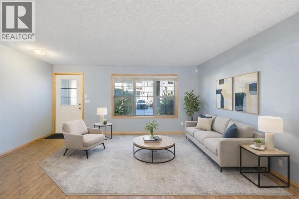Living room with light blue walls, grey carpet, a sofa, armchair, coffee table, and a window view. - 104, 23 Everridge Square Sw, Calgary