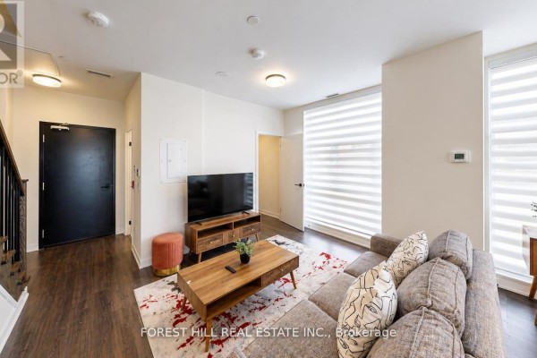 Living room with a grey sectional sofa, wooden coffee table, and large windows with blinds. - 104 - 16 Symes Road, Toronto