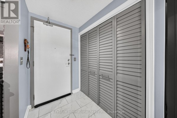 Apartment entrance with white door and double grey louvered closet doors. - 104 - 208 Silvercreek Parkway N, Guelph