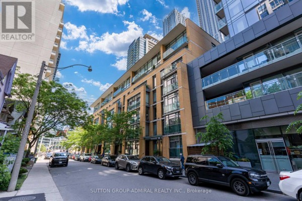 Street view of a brick apartment building with balconies and parked cars, under a blue sky. - 104 - 21 Scollard Street, Toronto