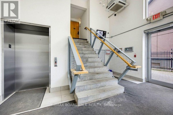 Interior hallway with a stainless steel elevator, concrete stairs, and metal railings. - 104 - 360 Cumberland Street, Ottawa