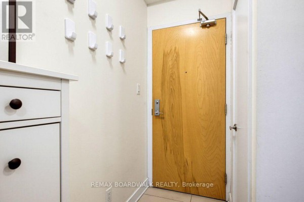 Entrance area to the apartment with a wooden door, white hooks, and a white cabinet. - 104 - 360 Cumberland Street, Ottawa
