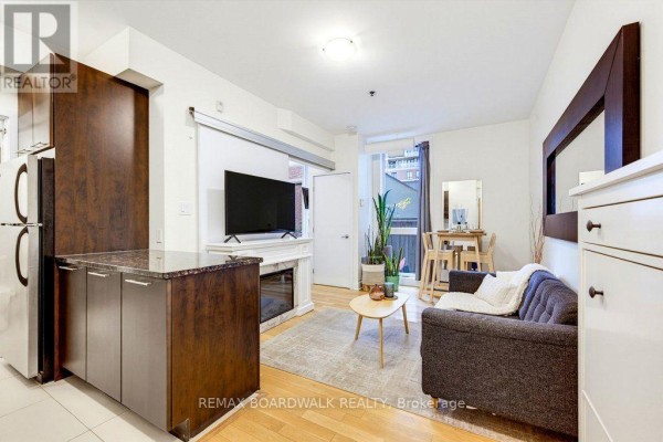 Living area showing a sofa, coffee table, fireplace, television, and dining table. - 104 - 360 Cumberland Street, Ottawa