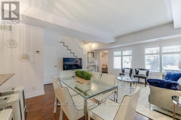 Open concept living and dining area with glass table, white chairs, and staircase. - 104 - 5 Richgrove Drive E, Toronto