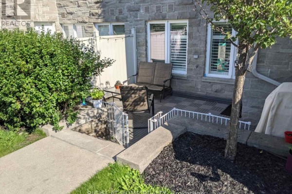 Small patio area with seating, stone flooring, and surrounded by greenery and stone facade. - 104 - 5 Richgrove Drive E, Toronto