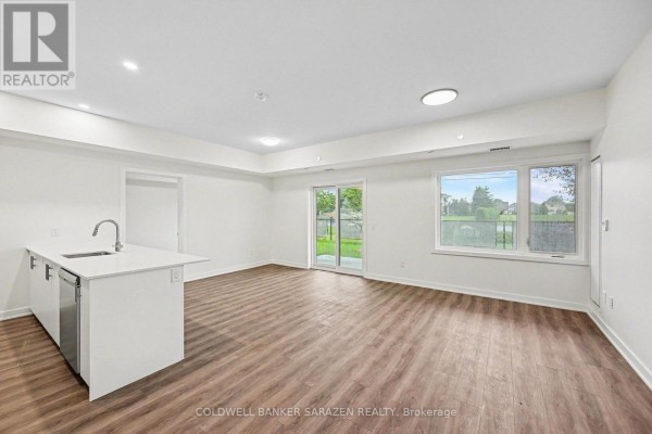 Living space with a patio door to a grassy yard, large windows, and light wood flooring. - 104 - 50 Corb Stewart Court, Arnprior