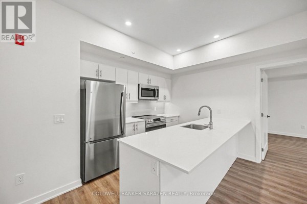 Contemporary kitchen with white cabinetry, stainless steel appliances, a quartz island, and light wood flooring. - 104 - 50 Corb Stewart Court, Arnprior