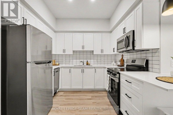 Modern white kitchen with stainless steel appliances and light wood flooring. - 104 - 5874 County Rd #19 Road, North Grenville