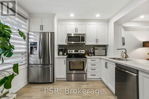 Close-up of a white kitchen with stainless steel refrigerator, oven, microwave, and dishwasher. - 104 - 6540 Falconer Drive, Mississauga