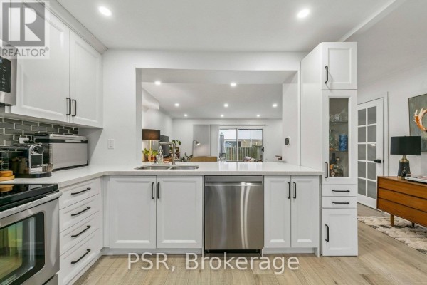 View of a white kitchen with a sink, dishwasher, and view into the living and dining area. - 104 - 6540 Falconer Drive, Mississauga