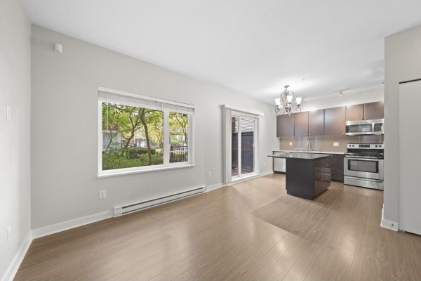 Living area with a window overlooking greenery, connected to the kitchen and dining space. - 104 13740 75a Avenue, Surrey