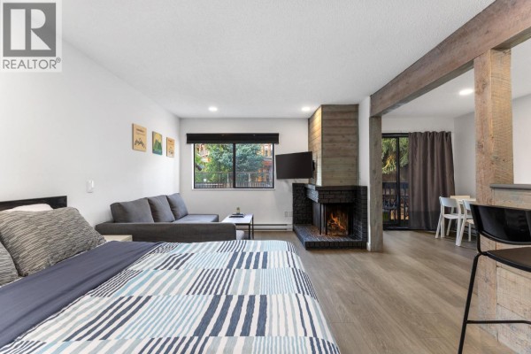 Studio apartment living space with a bed, sofa, fireplace, and dining area with chairs visible. - 104 2129 Lake Placid Road, Whistler