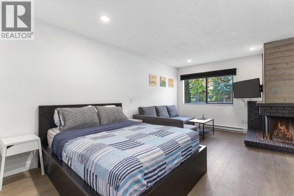 Studio bedroom with a queen bed, sofa, coffee table, and fireplace. Wood accents on ceiling beam and fireplace. - 104 2129 Lake Placid Road, Whistler